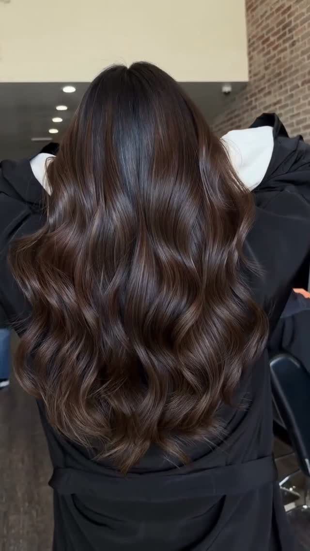 Glossy brunette waves cascade down a salon client's back