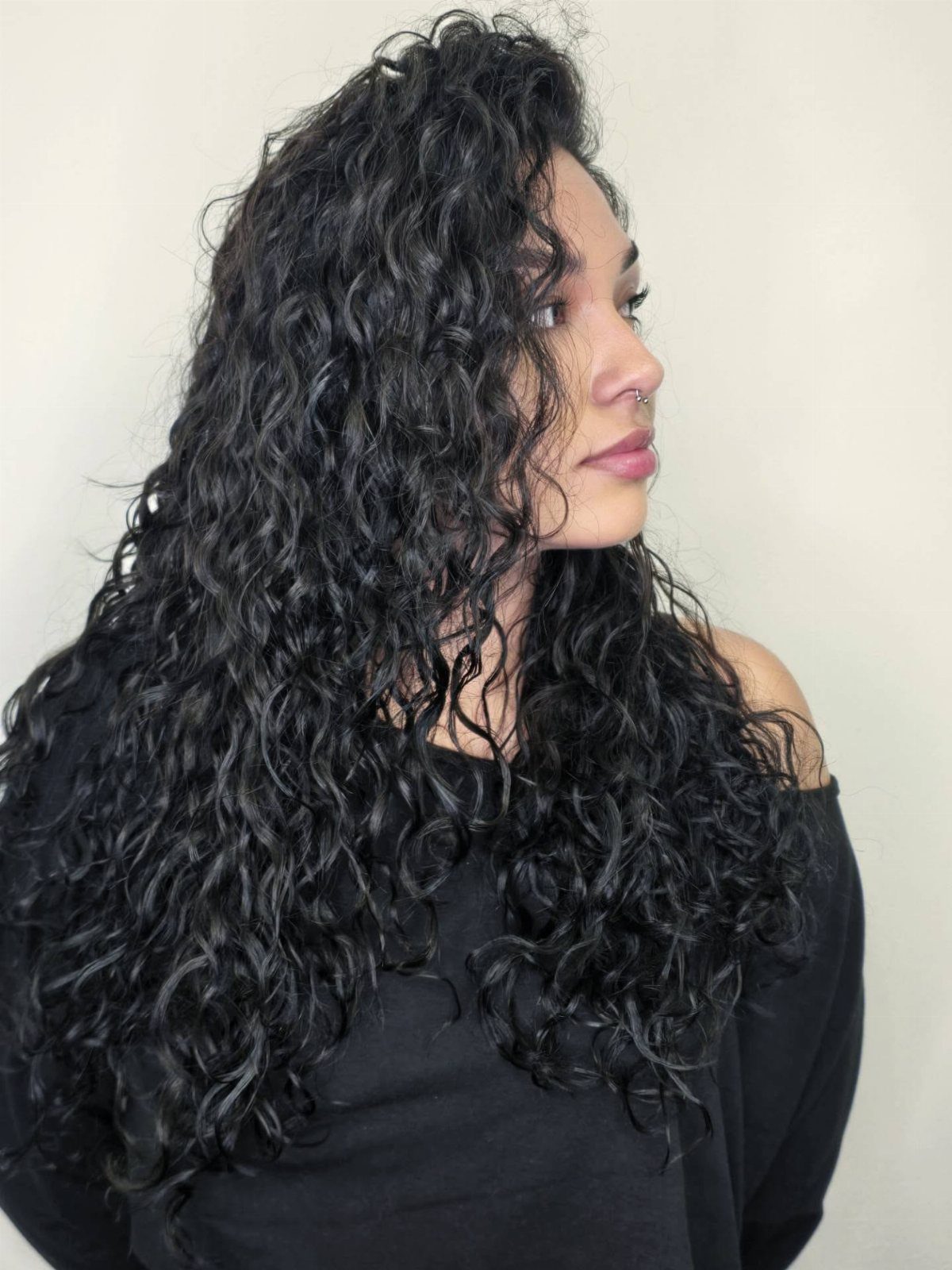 Woman with long dark natural curls wearing a black off-the-shoulder top