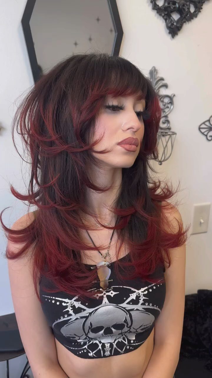 Woman poses showing long layered dark hair with deep red accents and wispy bangs