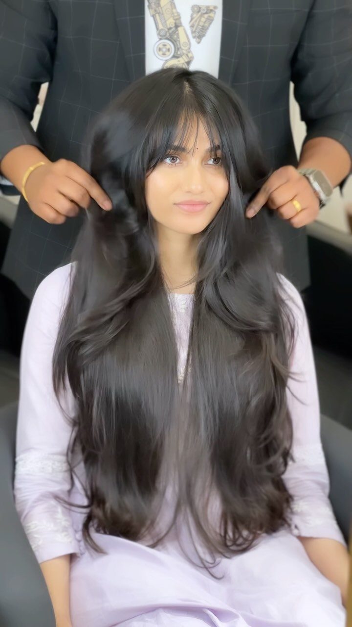 Woman with long dark waves and a full wispy fringe while her hair is arranged