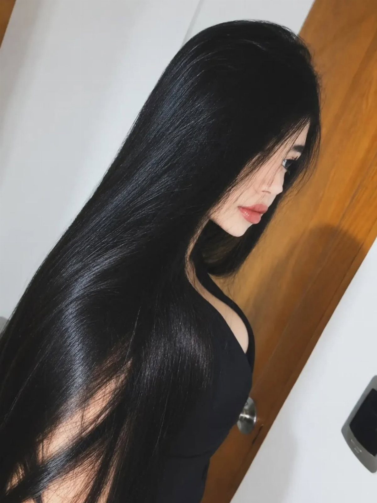 Woman with long glossy black hair worn loose and straight beside a wooden door