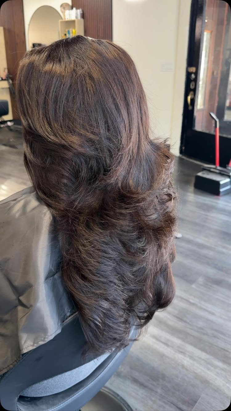 Long dark layered hair with voluminous, feathered ends in a salon