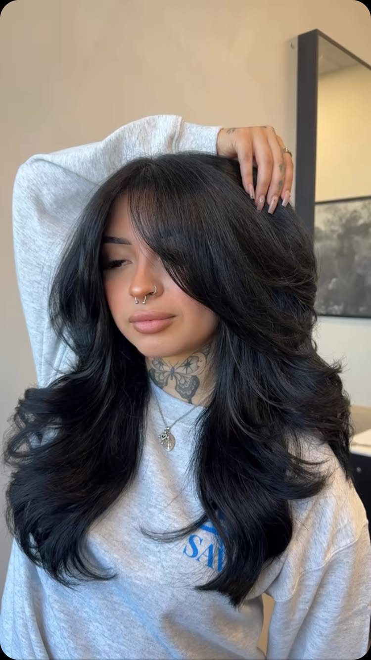 Long black layered hair falls in voluminous waves around a seated person’s shoulders.