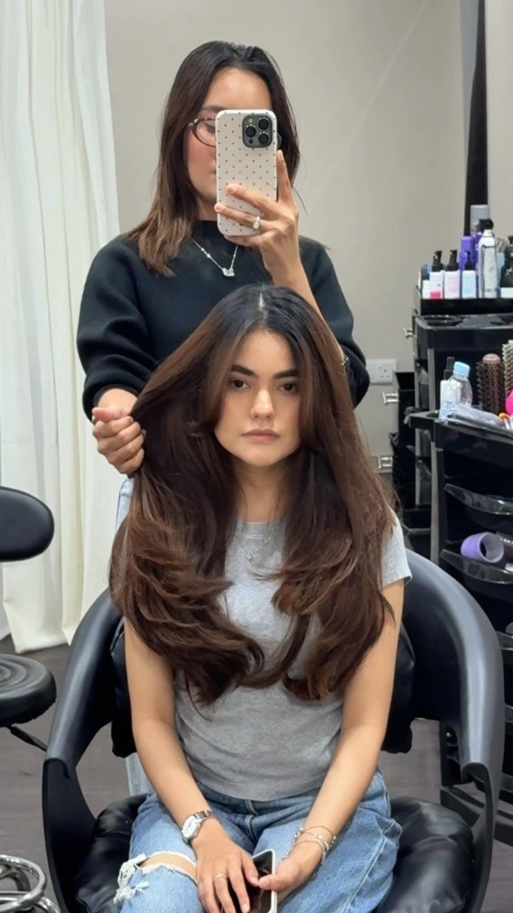 Woman with long dark brown hair and softly curled ends seated in a salon