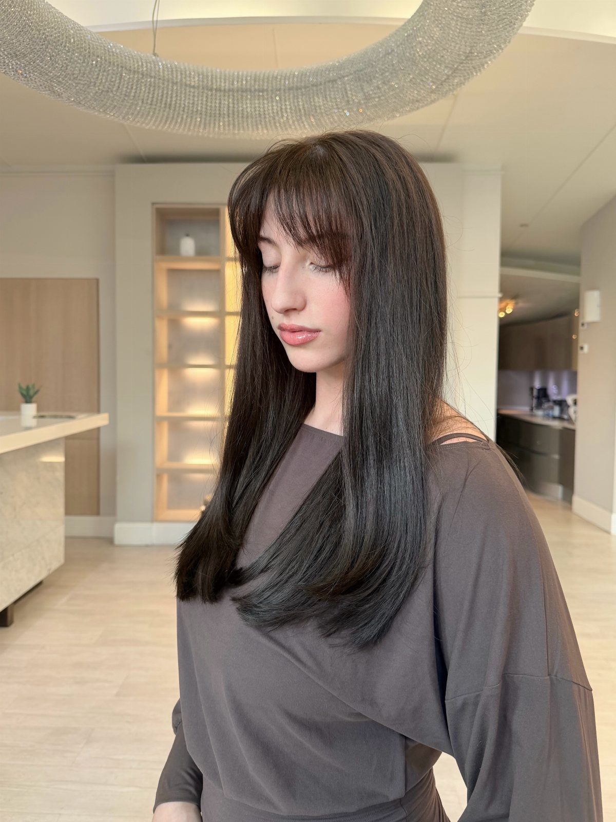 Woman with long dark hair and soft wispy bangs in a salon