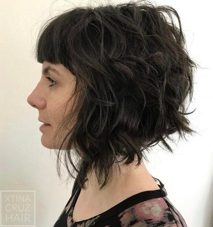 Dark curly bob with wispy bangs shown in a side-profile portrait
