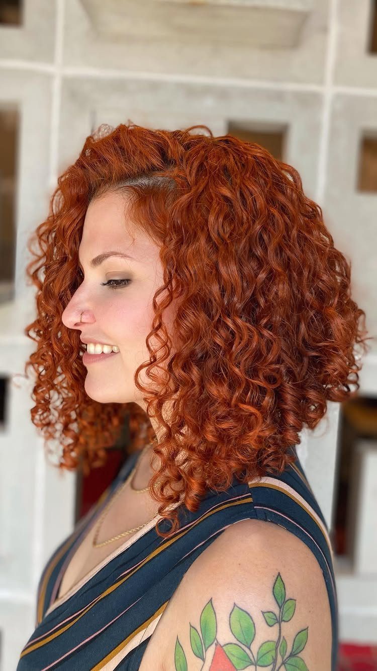 Woman with curly copper hair, shorter rounded back, and longer face-framing curls