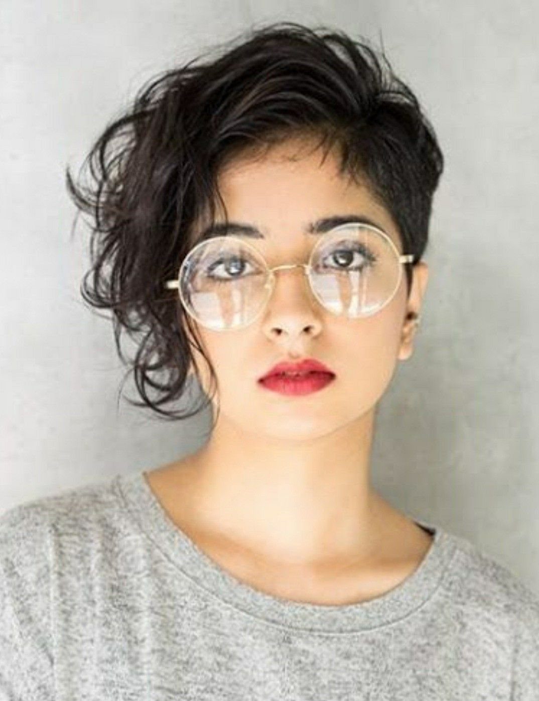 Side-swept dark wavy haircut frames a person’s face with clear glasses