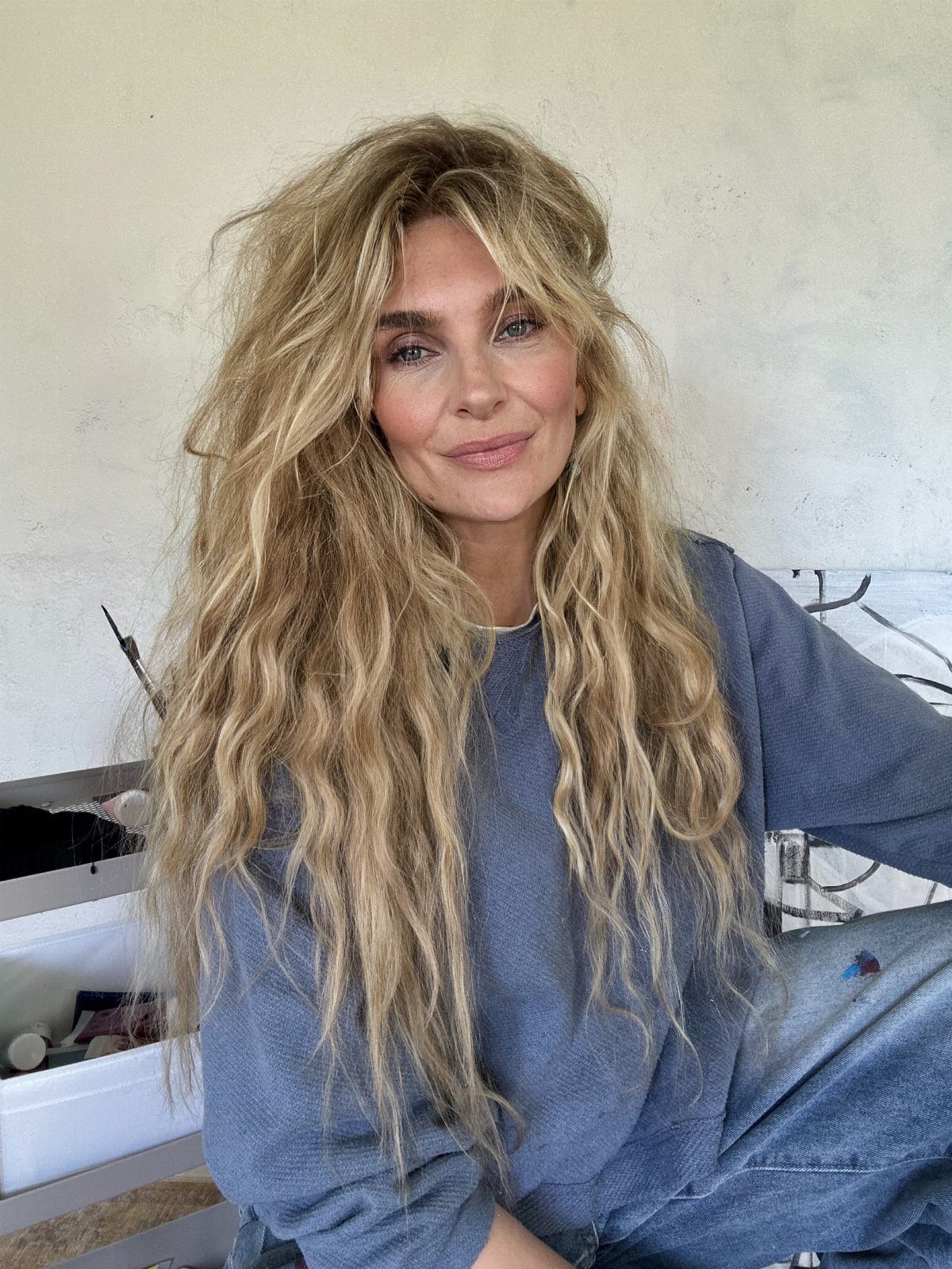 Woman with long blonde waves and a loose center-parted fringe in a salon