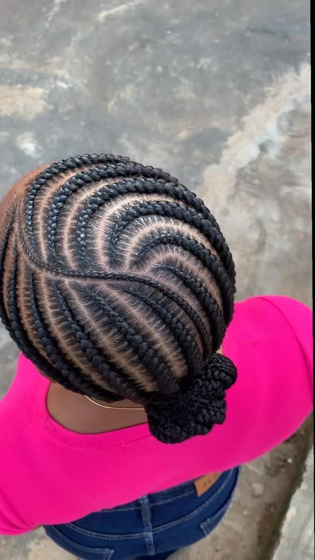 Cornrow braids gathered into a bun on a person wearing a pink top
