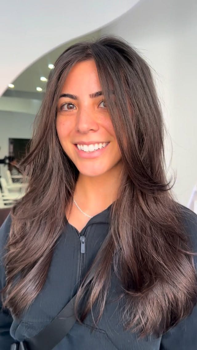 Woman smiling with long dark face-framing layers in a bright salon