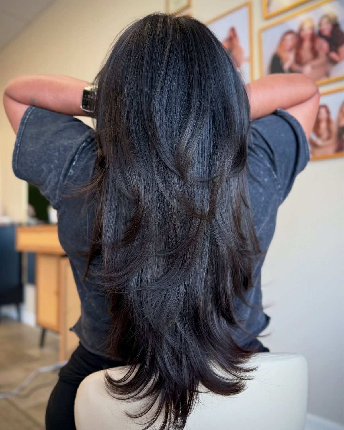 Long, thick dark hair falls in layered sections with curled-under ends