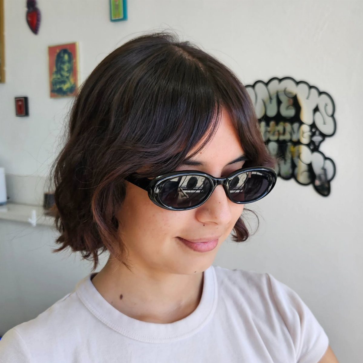 Person in sunglasses showing a dark, tousled chin-length bob with side-swept bangs