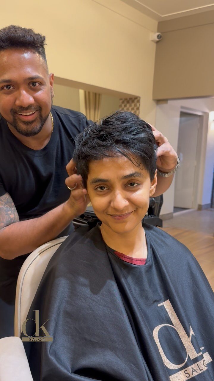 Person with a short dark pixie cut sits in a salon chair