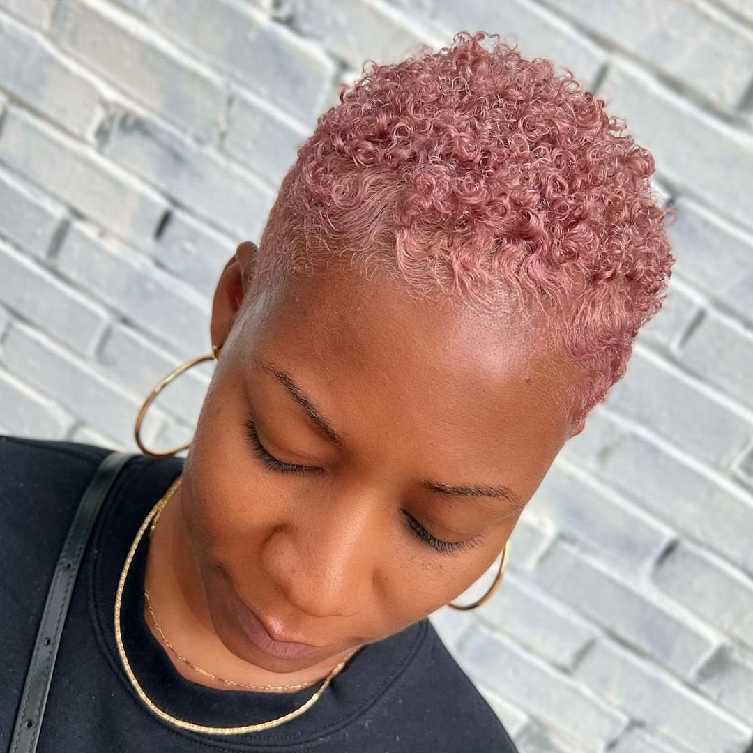 Short tightly curled pink hair shown from above against a gray brick wall