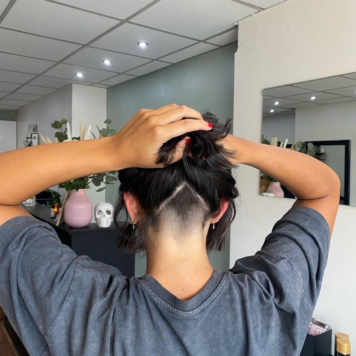 Dark-haired person lifts long hair to show a closely shaved nape undercut