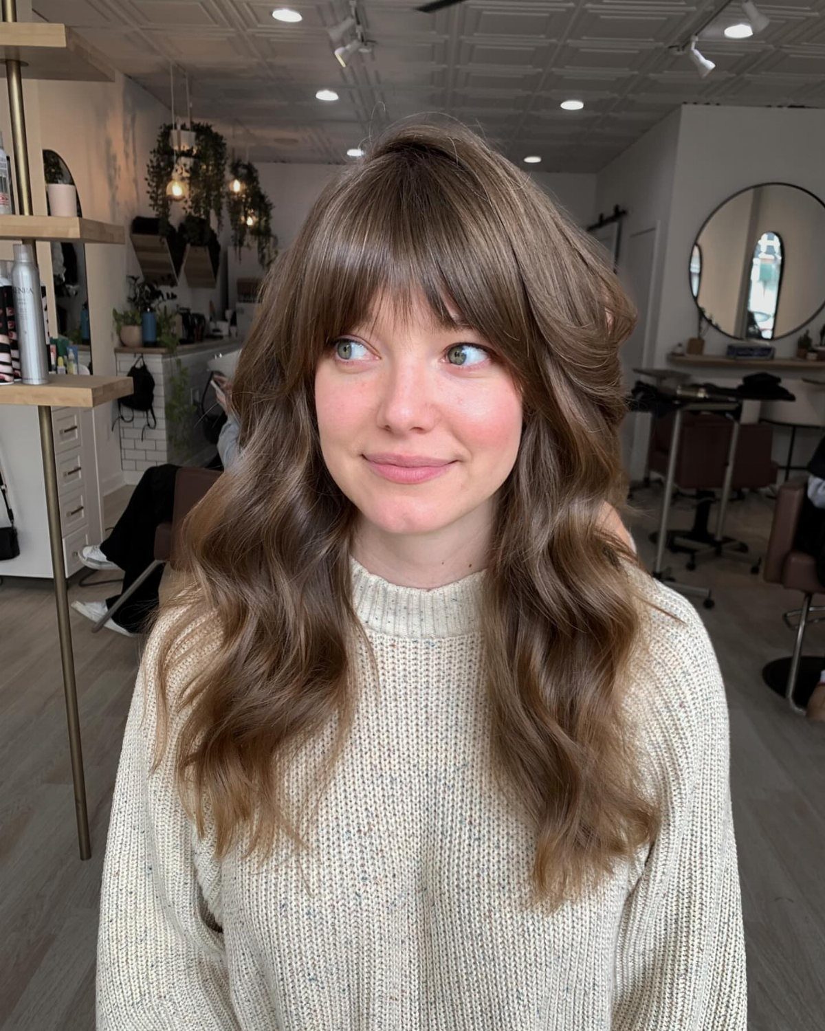 Woman with wavy light brown hair and curtain bangs seated in a salon