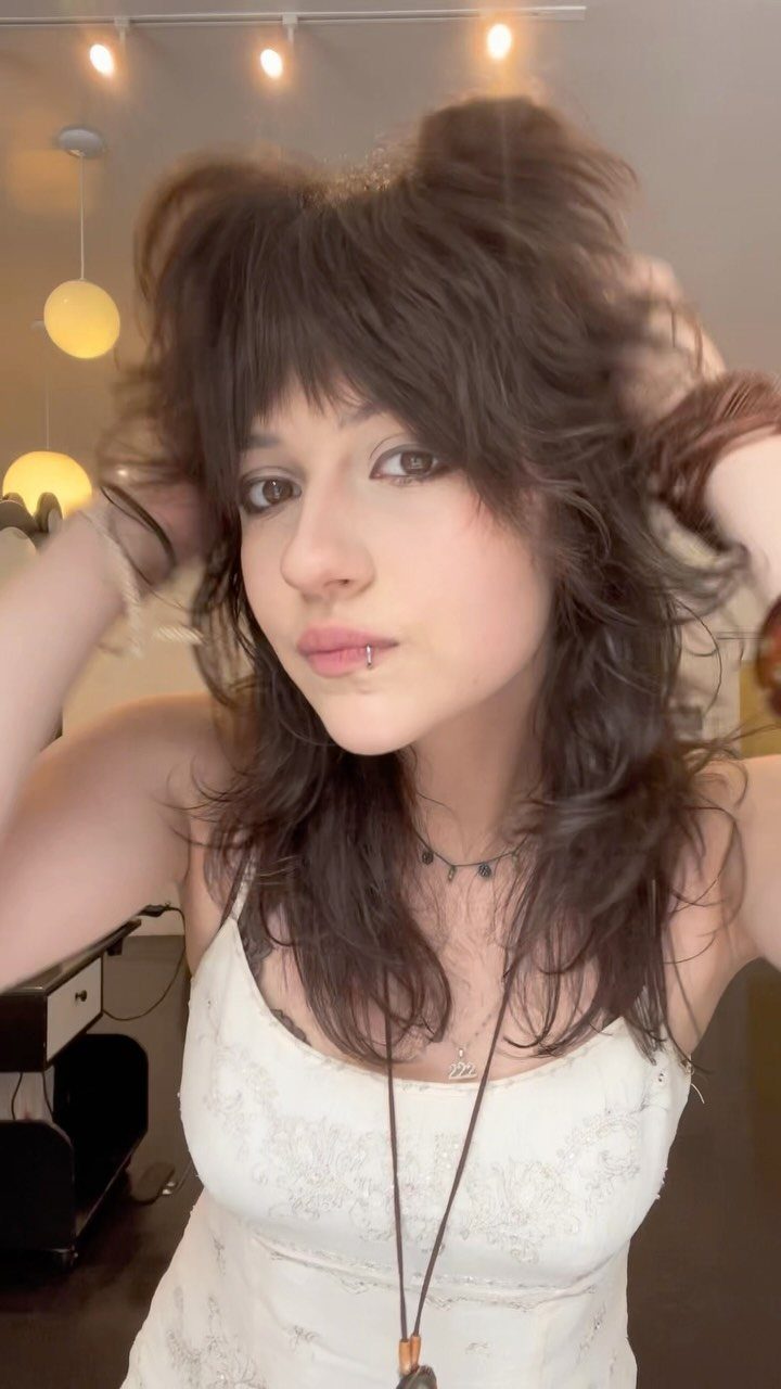 Person with feathered bangs and tousled layered brown hair in a white top