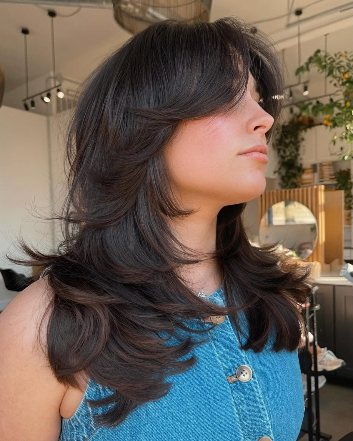 Woman with dark layered hair, sweeping bangs, and curled flipped ends in a salon