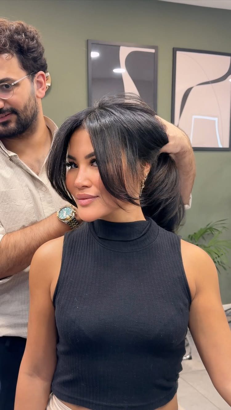 Woman with a dark layered medium haircut and long side-swept bangs in a salon