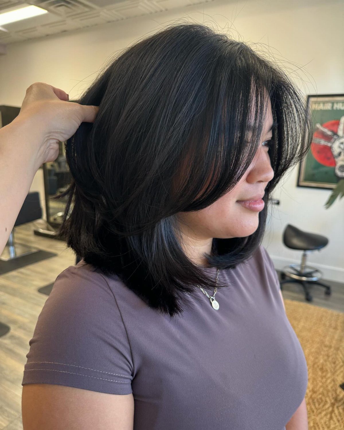 Shoulder-length dark layered bob with long side-swept bangs in a salon