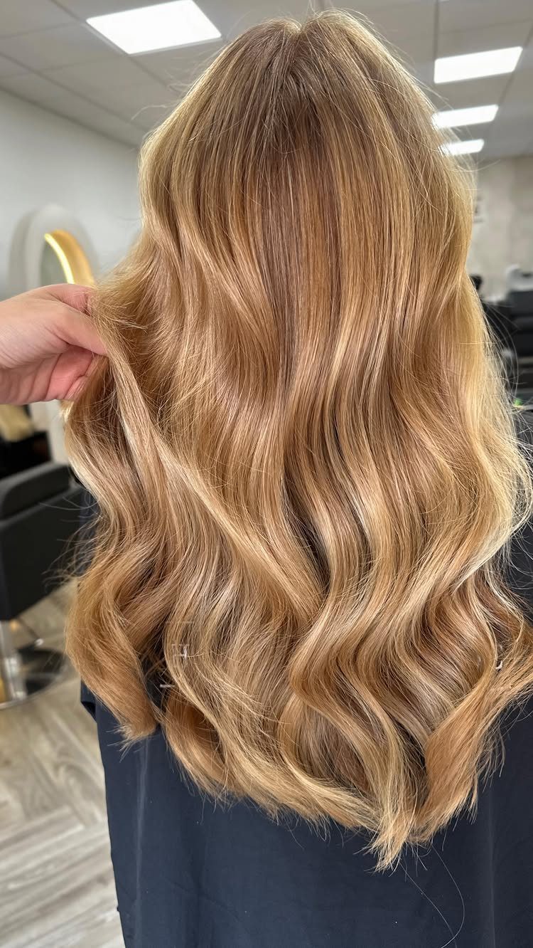 Long golden blonde hair falls in loose layered waves over a dark salon cape