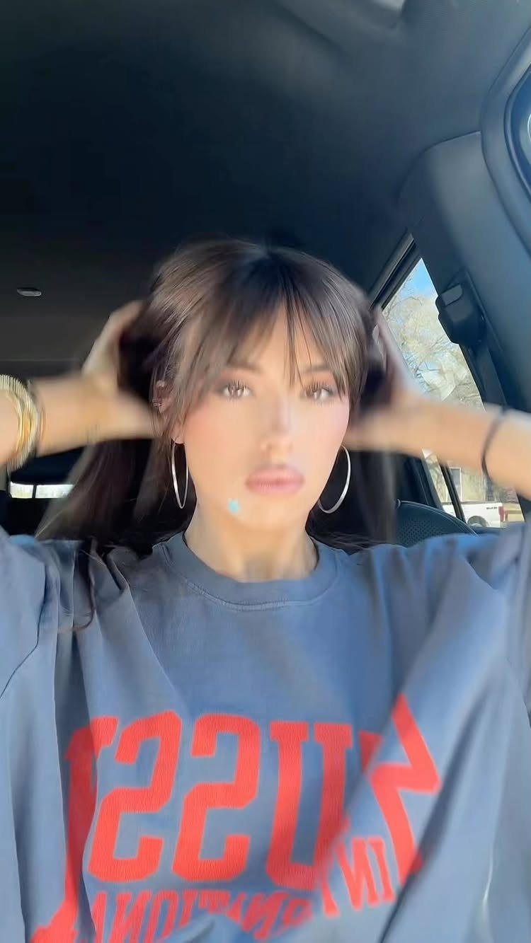 Woman displays wispy bangs and loose dark layers in a car