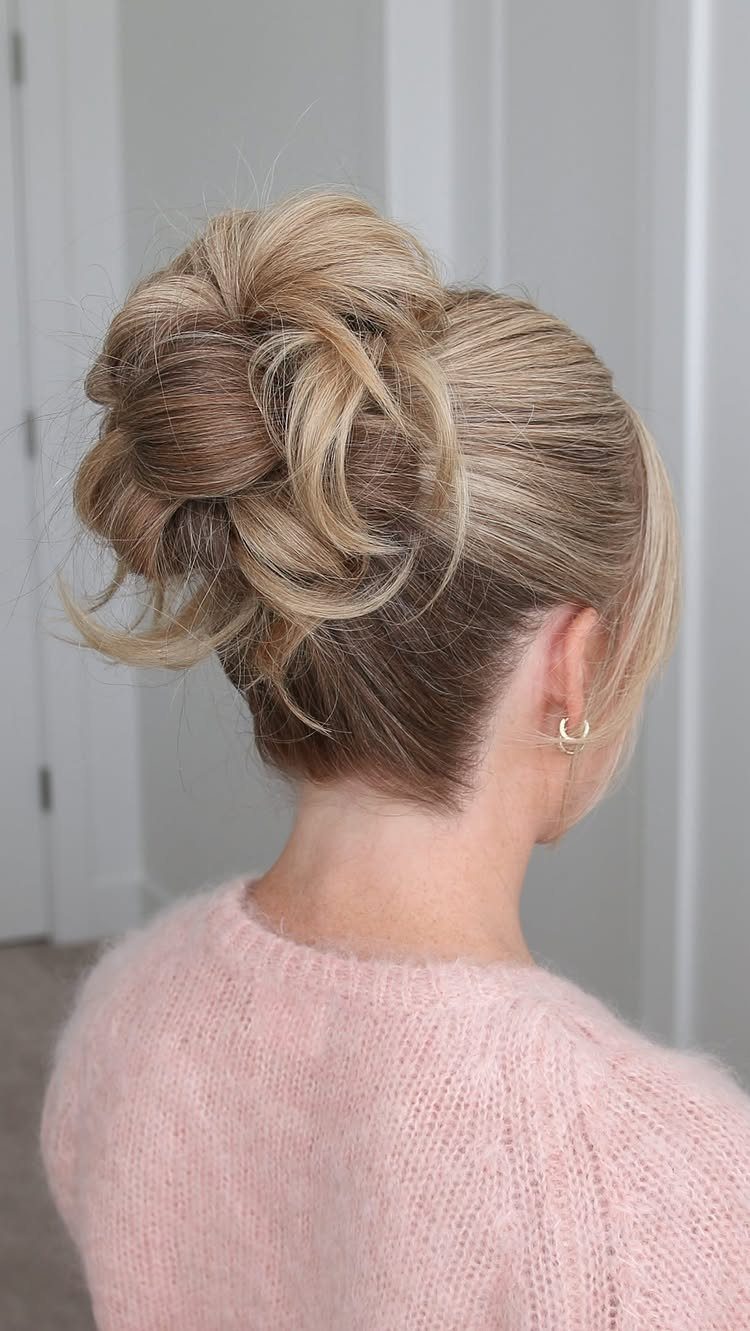 Loose blonde bun with wispy strands on a person in a pink sweater