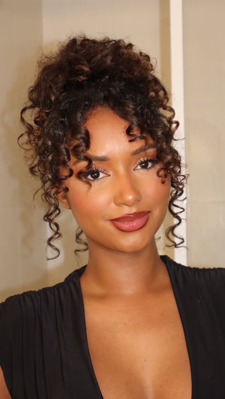 Woman wearing a curly high messy bun with loose face-framing tendrils