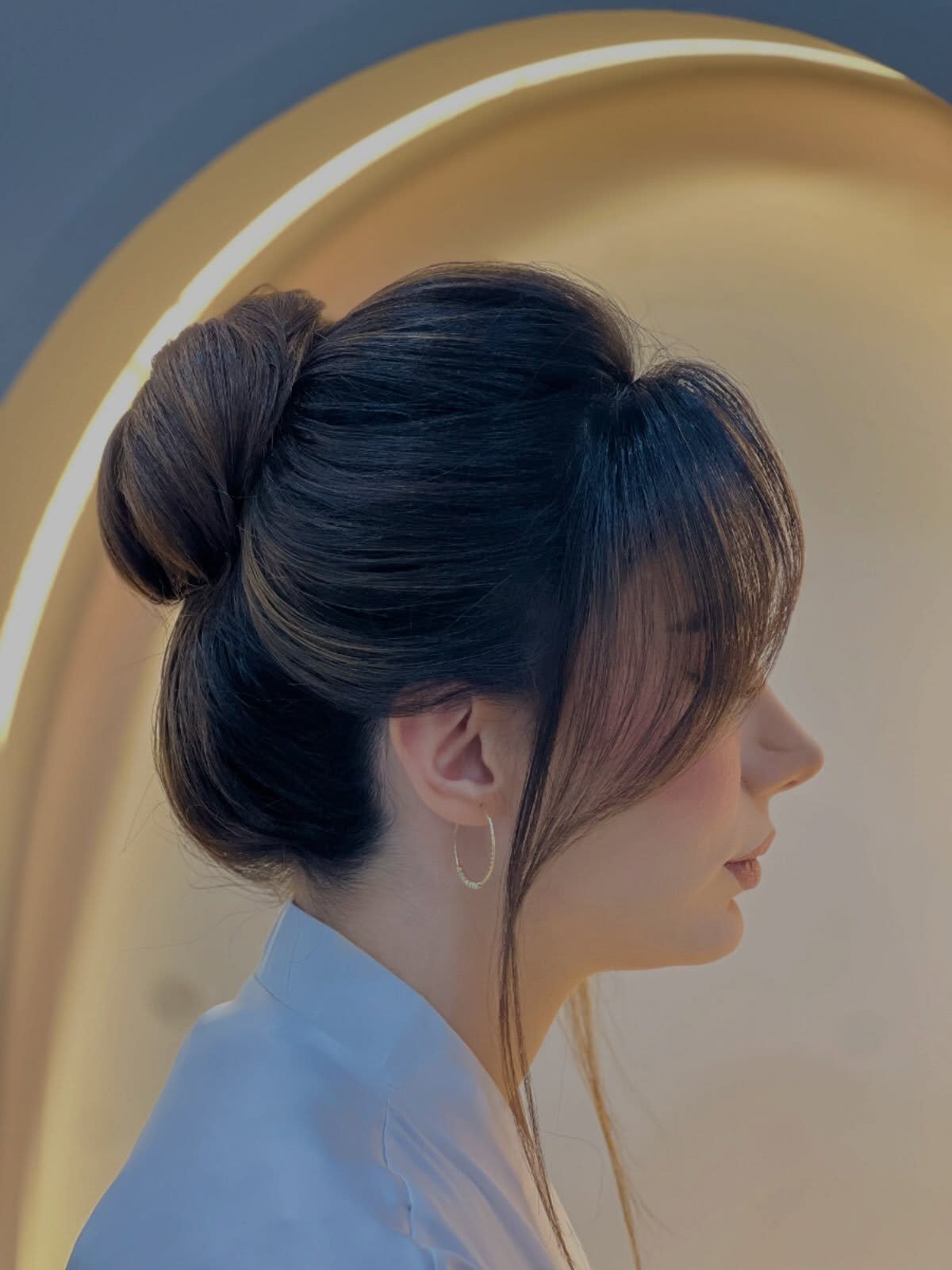 Woman with a rounded bun, long side-swept bangs, and face-framing strands