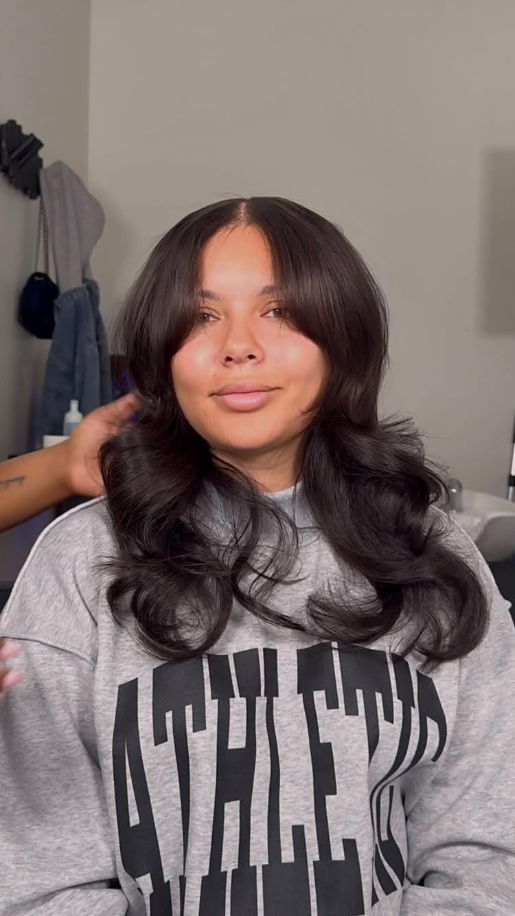 Curtain bangs frame a person’s face above long, curled dark hair