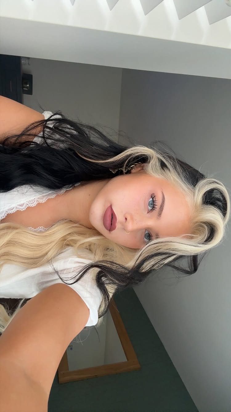 Woman posing with long wavy hair split into black and platinum blonde sides