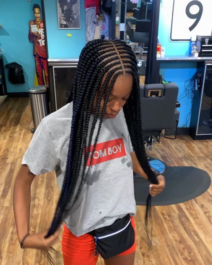 Long micro braids fall from a neat middle part over a gray T-shirt.