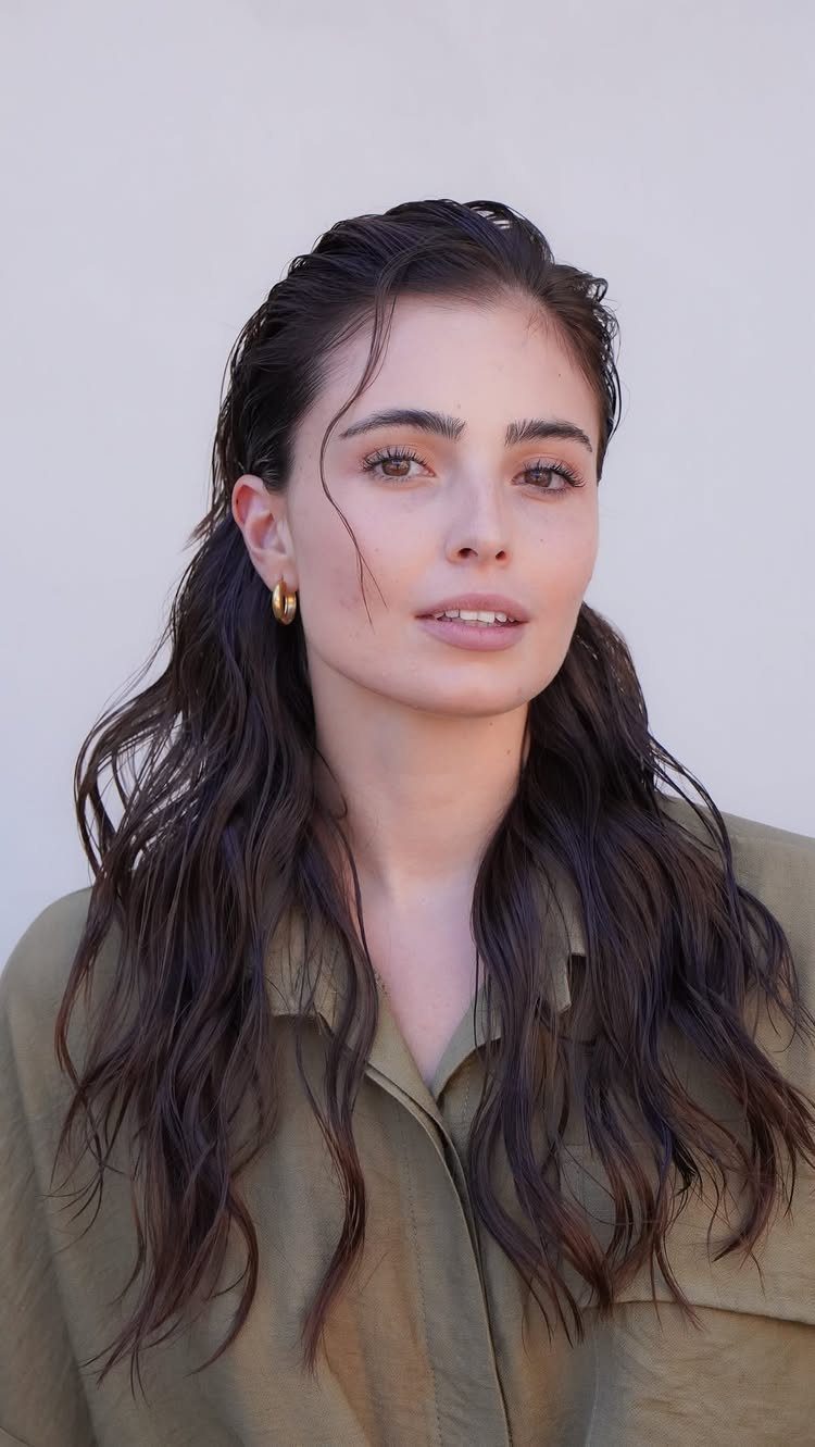 Woman with long dark wet-looking waves and loose strands framing her face
