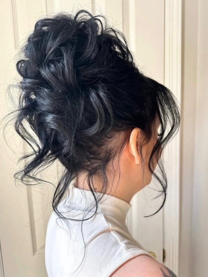 Dark curled updo with loose side bangs against a pale paneled door