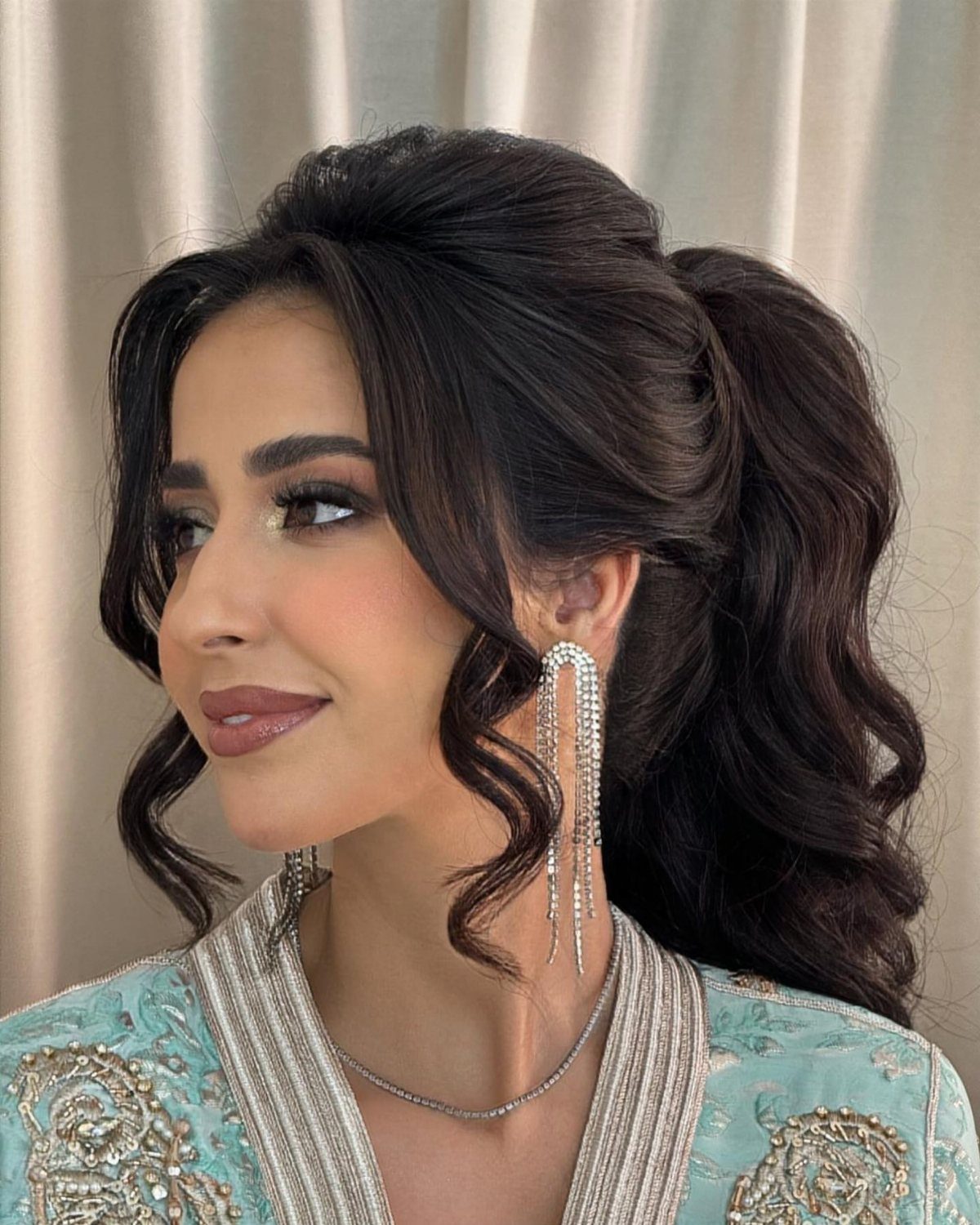 Woman wearing a high curly ponytail with loose face-framing tendrils
