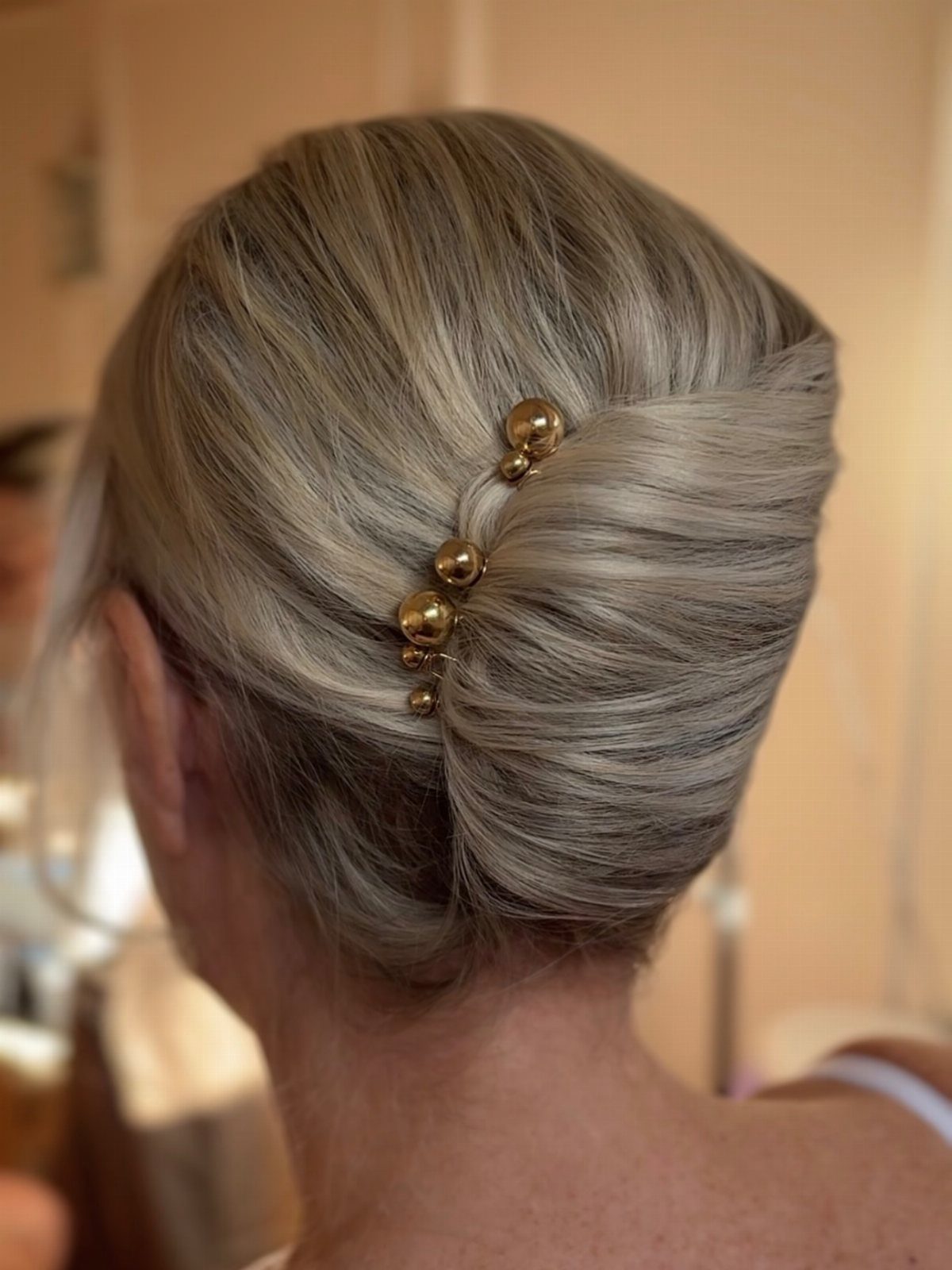 Silver-gray hair swept into a smooth French twist with gold pins