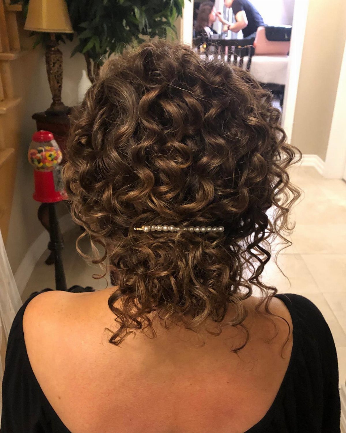 Loose curly updo secured with a jeweled clip, with ringlets framing the nape