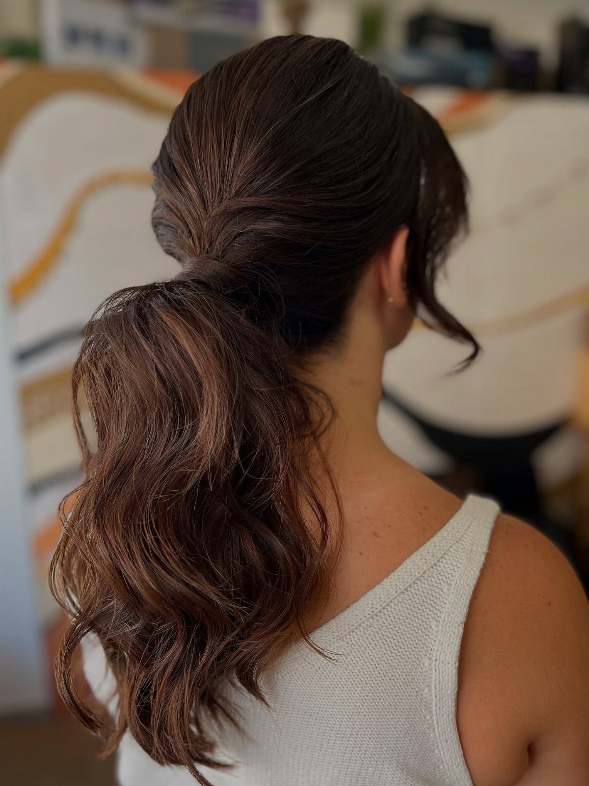 Dark brown low ponytail with loose curls on a woman in a white top