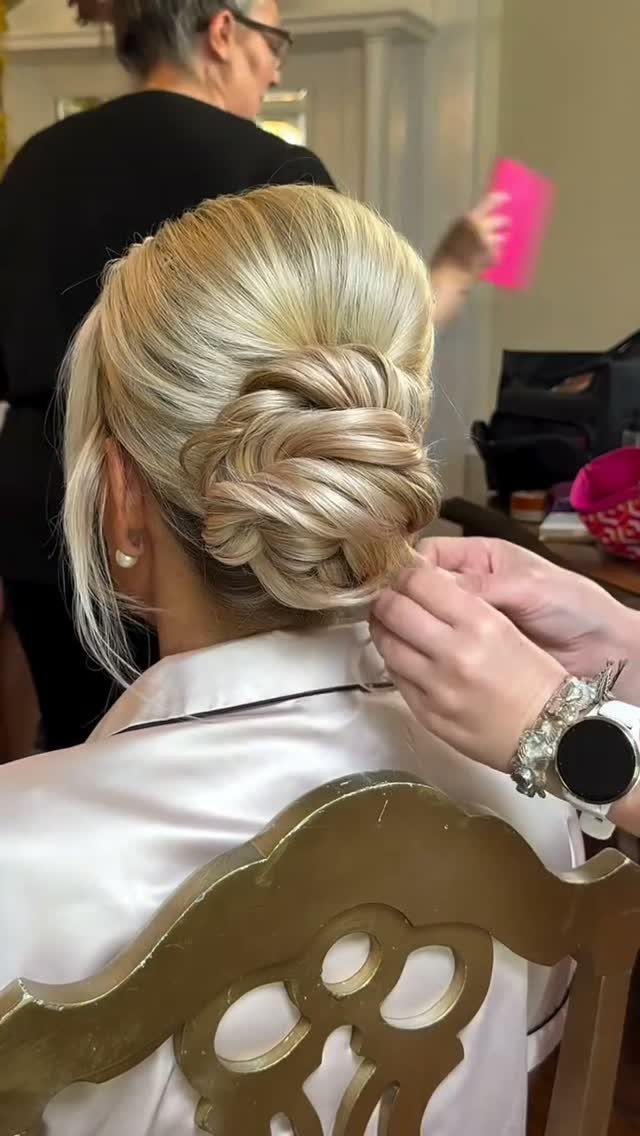 Blonde woven updo with loose strands being arranged by a stylist