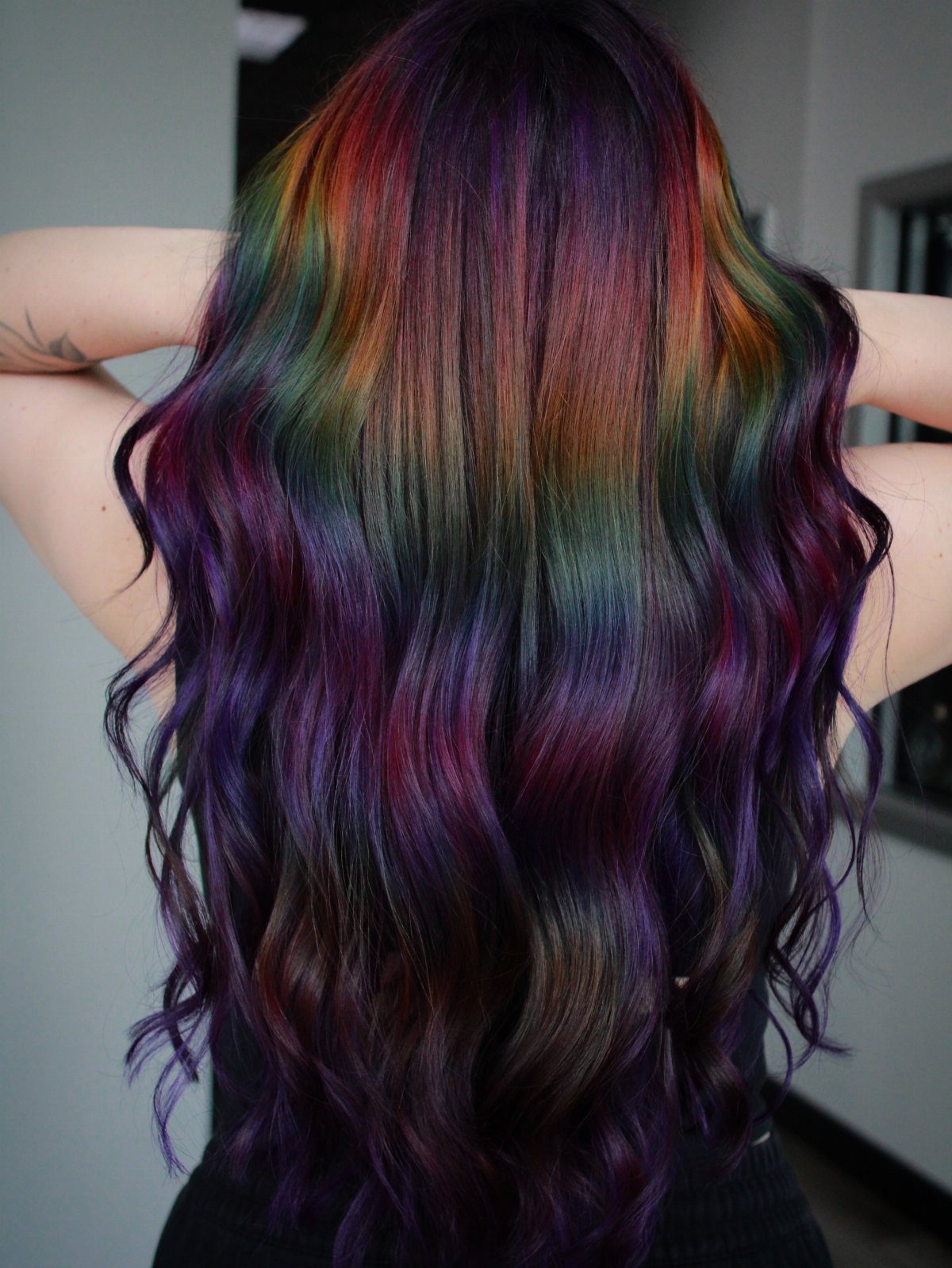 Long wavy dark hair with rainbow streaks concentrated near the crown and scattered through the lengths