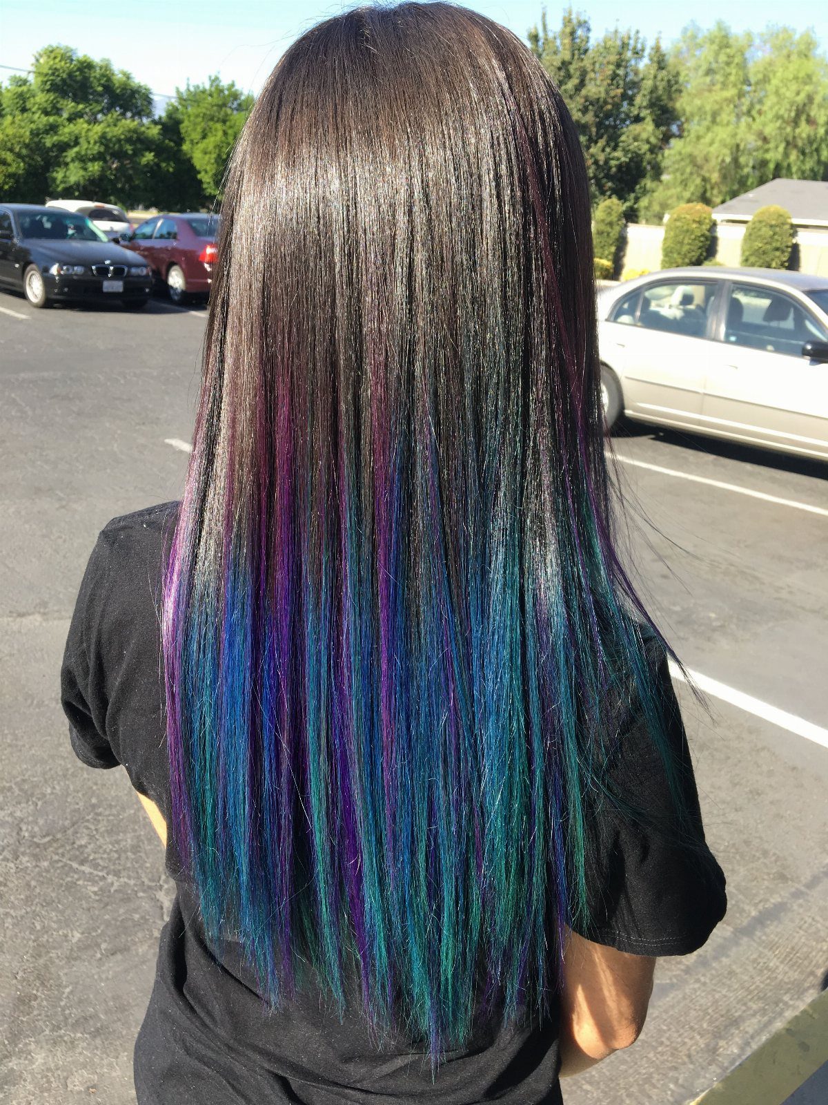 Long dark hair with teal, blue, and purple streaks in a sunny parking lot