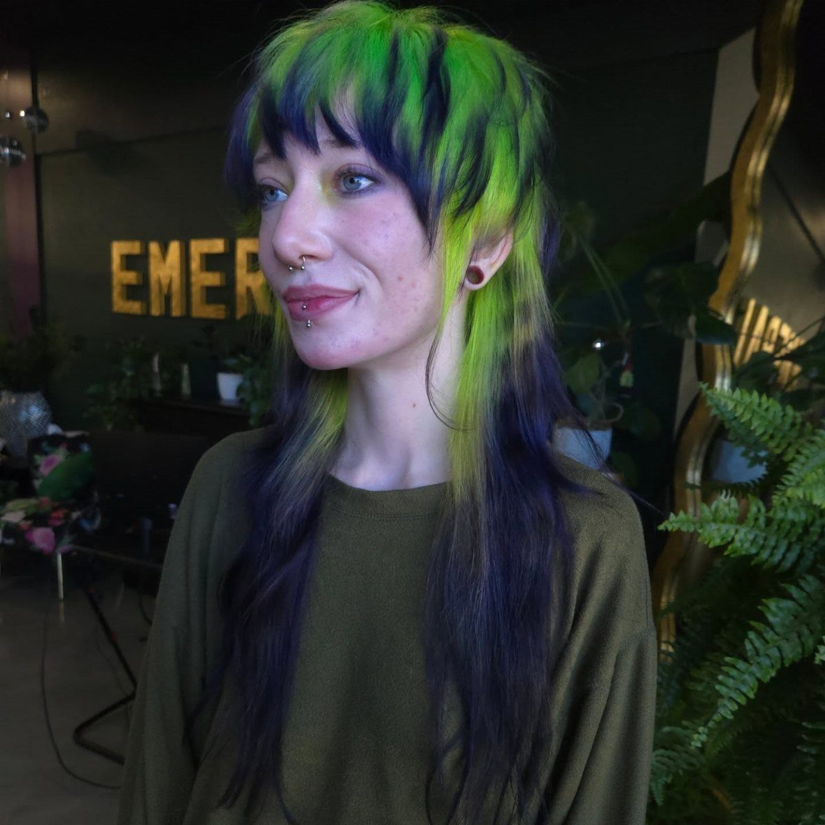 Long dark hair with bright green, teal, and purple highlights frames a woman's face.