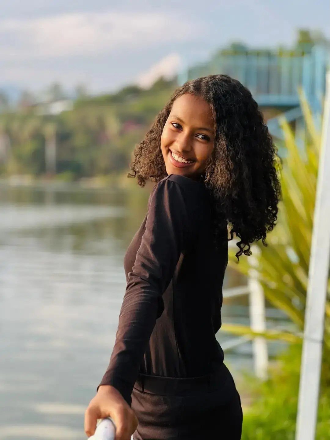 Girl smiling with long natural curls worn loose beside the water