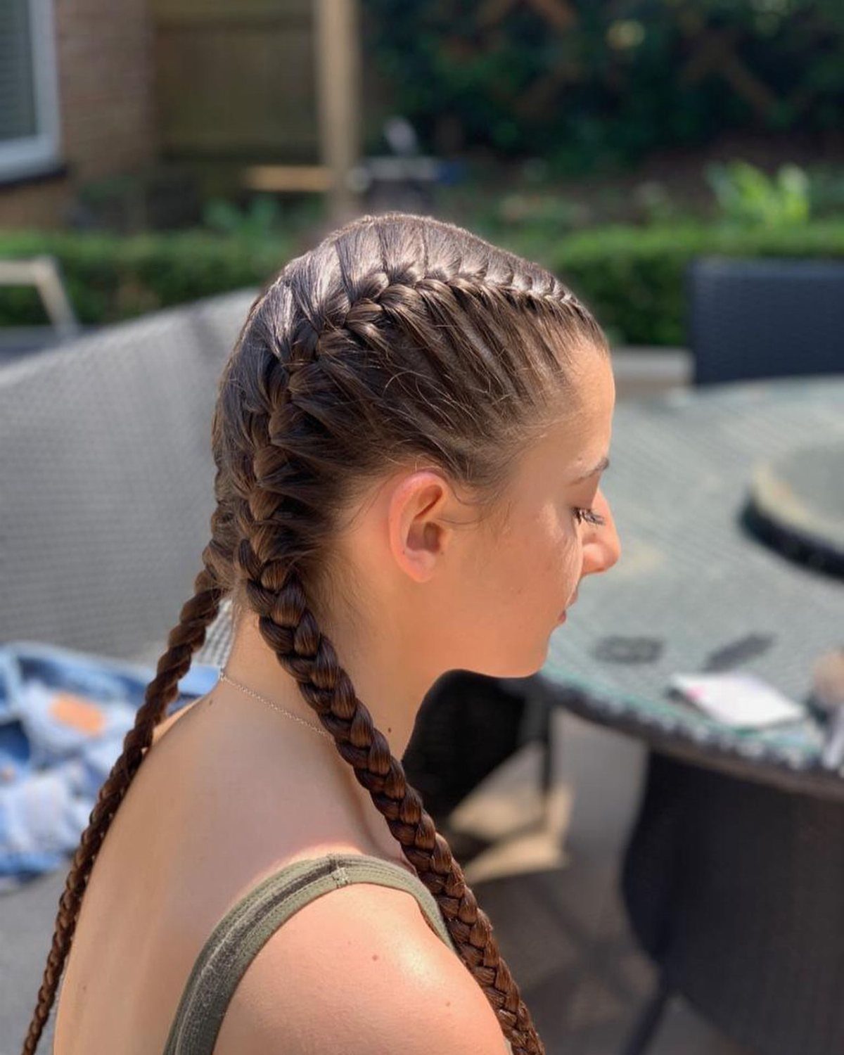 Girl showing two long Dutch braids outdoors from a side view