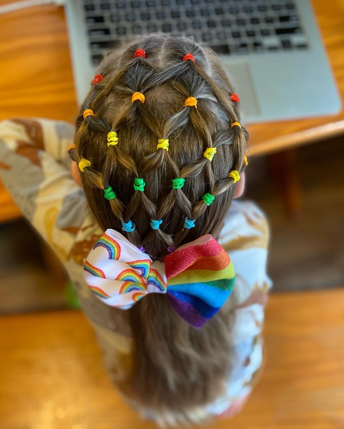 Child’s brown hair in rows of colorful elastic-secured sections with a rainbow bow
