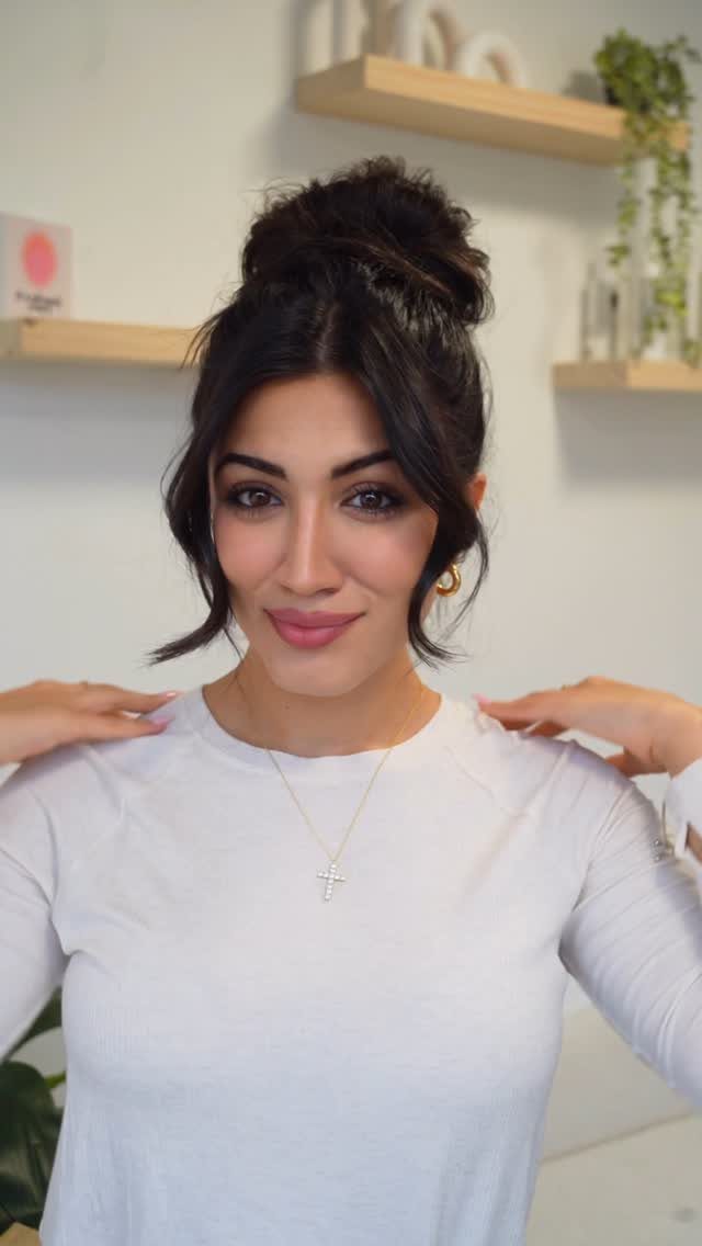 Woman posing with a high, loose bun and face-framing strands