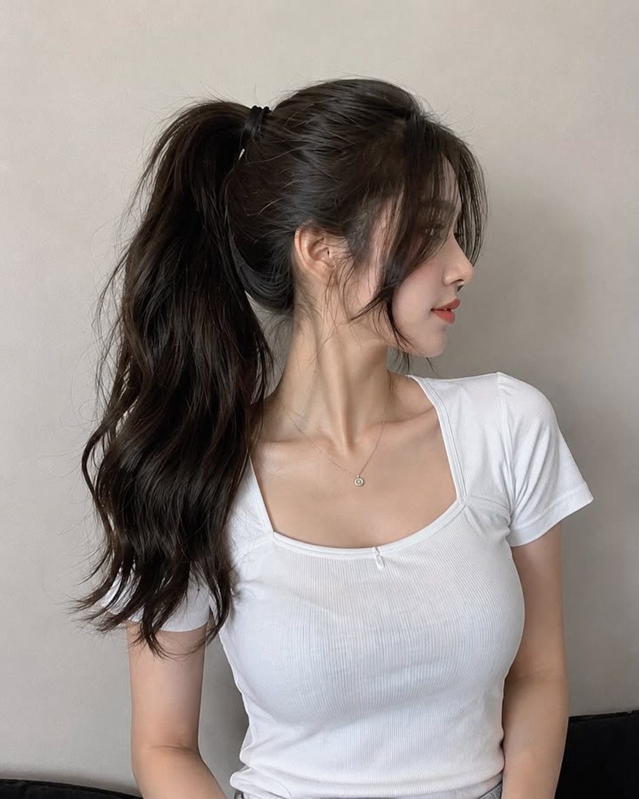 Woman with a high dark ponytail and loose strands poses in profile