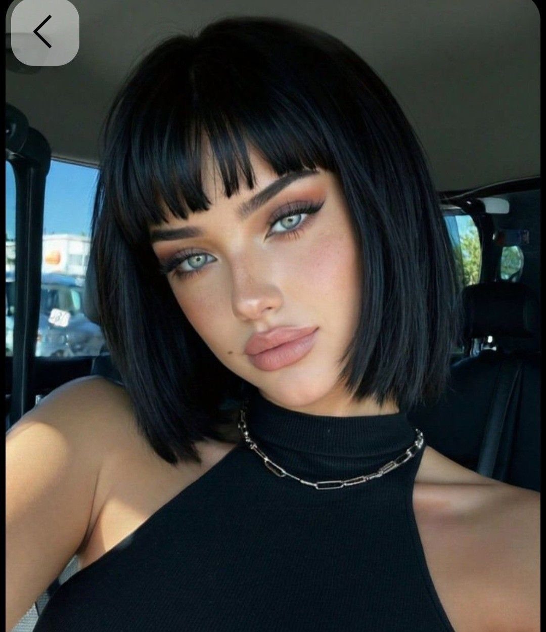 Woman posing in a car with a glossy black bob and blunt bangs