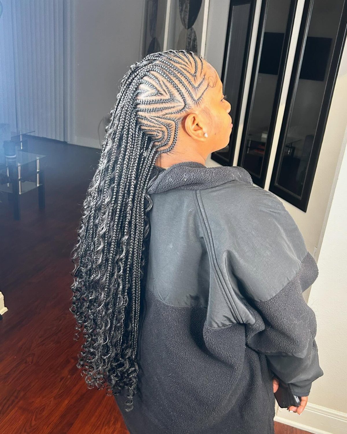 Long black braids cascade from intricate geometric cornrows along one side of her head